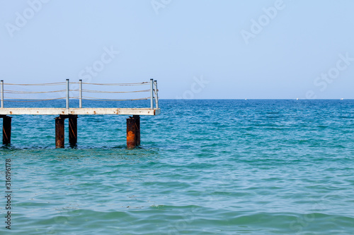 Fragment of an old pier against the background of the blue sea and cloudless sky. Romance of distant wanderings.