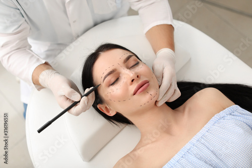 Plastic surgeon applying marks on patient's face in clinic