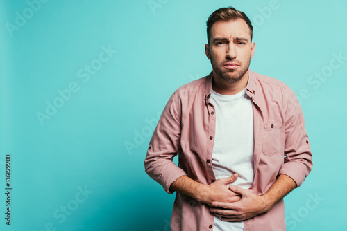 upset handsome man having abdominal pain, isolated on blue