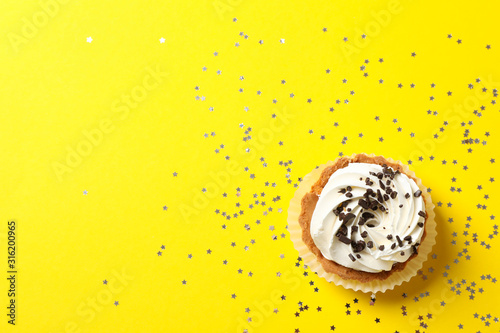 Cupcake and glitter stars on yellow background, top view