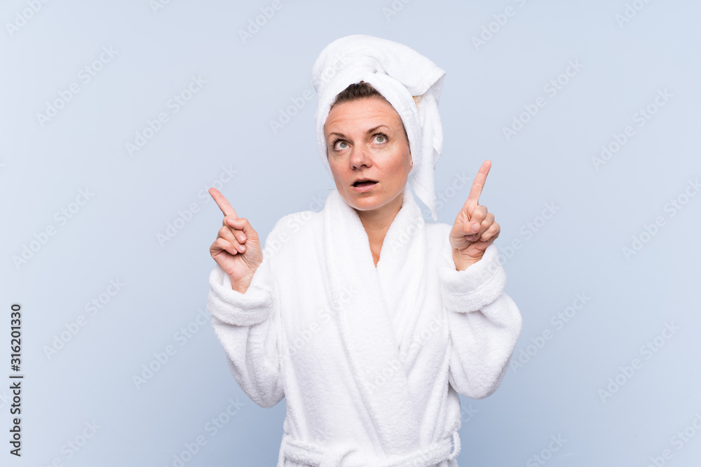 Woman in bathrobe over isolated blue background pointing with the index finger a great idea