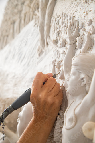 Close up of man ceramist hands holding a tool and working on sculpture details in workshop.