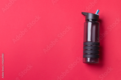 black plastic sport bottle lying on right side of red background with copy space