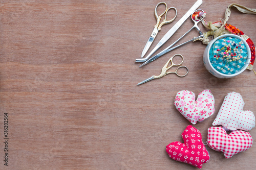 Flat lay Crafts made with fabric is a heart shape with sewing tools and accessories on a wooden background.