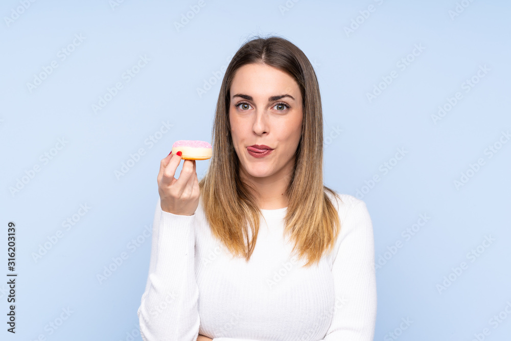Young blonde woman over isolated blue background holding a donut Young blonde woman over isolated blue background holding a donut