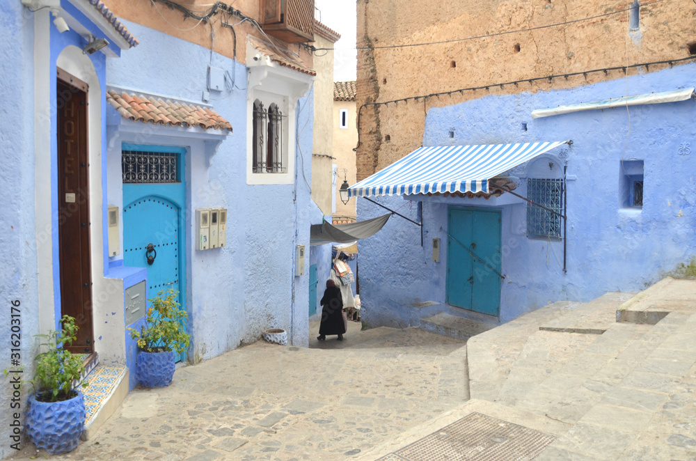 An arabic woman walking toward the end of the old town at  Chefchaouen old medina.