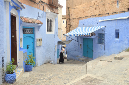 An arabic woman walking toward the end of the old town at  Chefchaouen old medina. © peacefoo