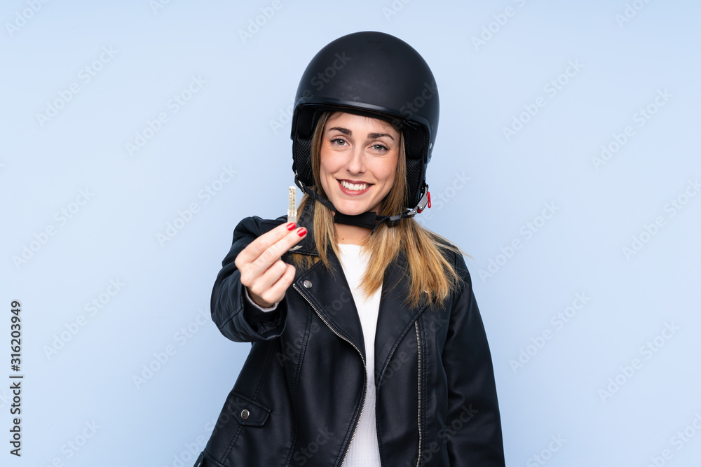 Young blonde woman with a motorcycle helmet and a key over isolated blue background Young blonde woman with a motorcycle helmet and a key over isolated blue background
