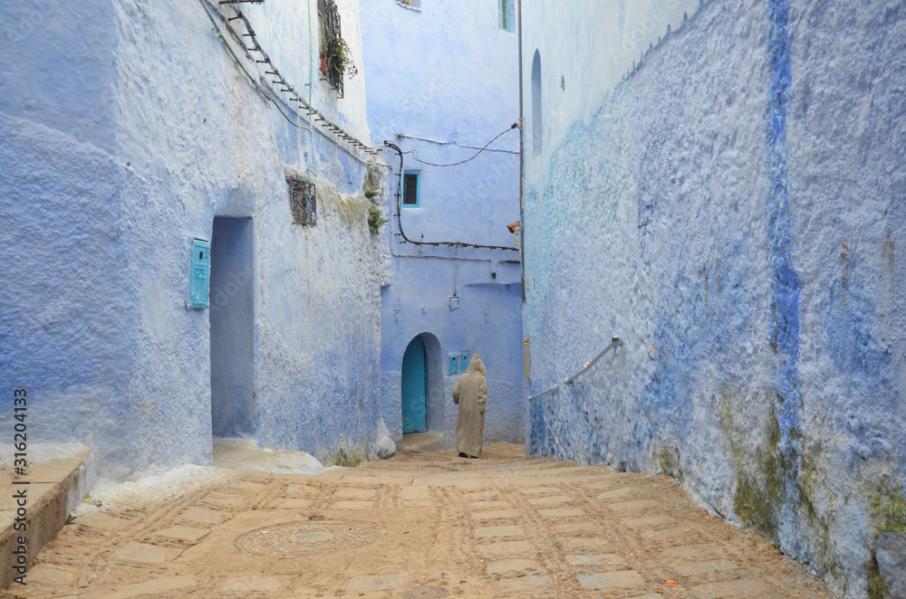 Man in traditional Djellabah walking in the Chefchaouen old medina.