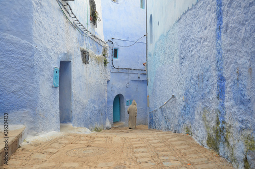 Man in traditional Djellabah walking in the Chefchaouen old medina. © peacefoo
