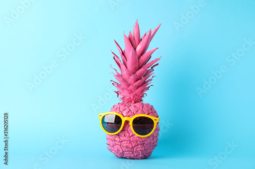 Painted pink pineapple with sunglasses on blue background, space for text