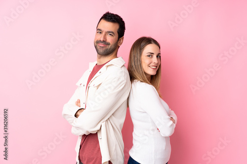 Couple in Valentine Day over isolated pink background keeping the arms crossed in lateral position while smiling