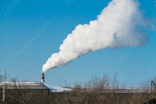 Industrial pipe with dense white smoke on blue sky background