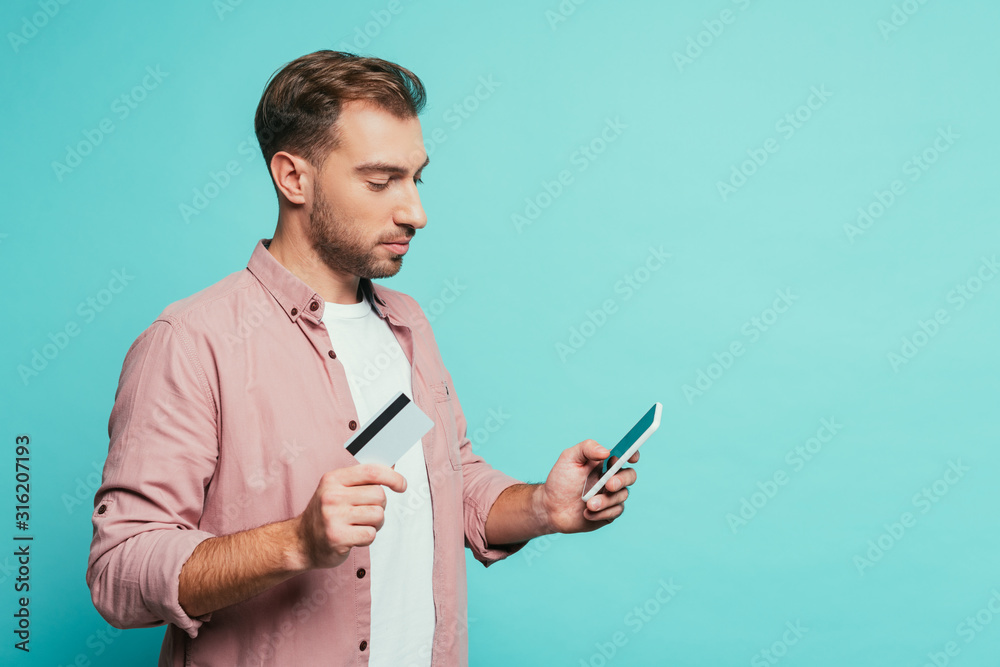 upset man shopping online with smartphone and credit card, isolated on blue upset man shopping online with smartphone and credit card, isolated on blue