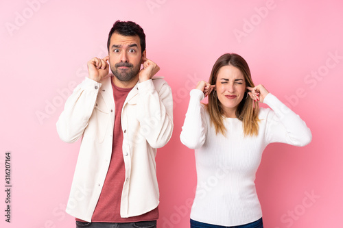 Couple in Valentine Day over isolated pink background covering both ears with hands