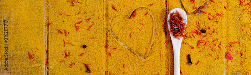 Banner with Heart of spices and seasonings. White spoon with saffron on curry background.