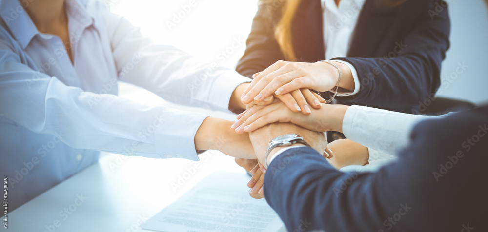 Business team showing unity with their hands together in sunny office. Group of people joining hands and representing concept of friendship, teamwork and partnership Business team showing unity with their hands together in sunny office. Group of people joining hands and representing concept of friendship, teamwork and partnership