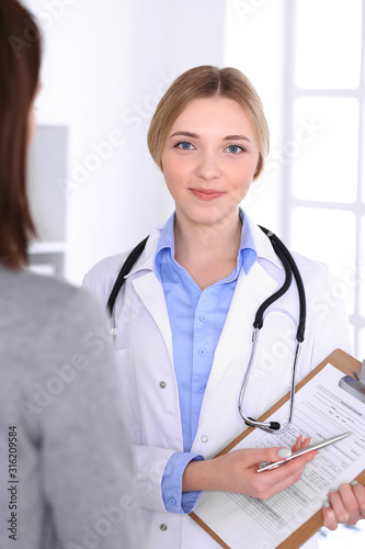 Young woman doctor and patient at medical examination at hospital office. Blue color blouse of therapist looks good. Medicine and healthcare concept