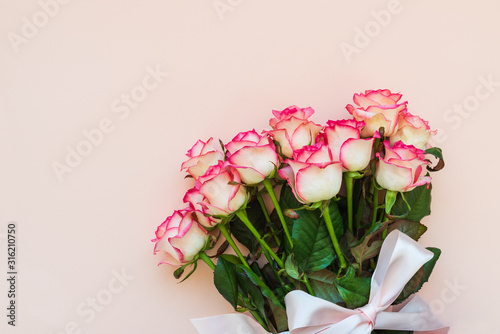 Bouquet of fresh pink roses wrapped pink ribbon on pink background. Top view. Flat lay. Copy space. Valentines day, mothers day or birthday celebration concept