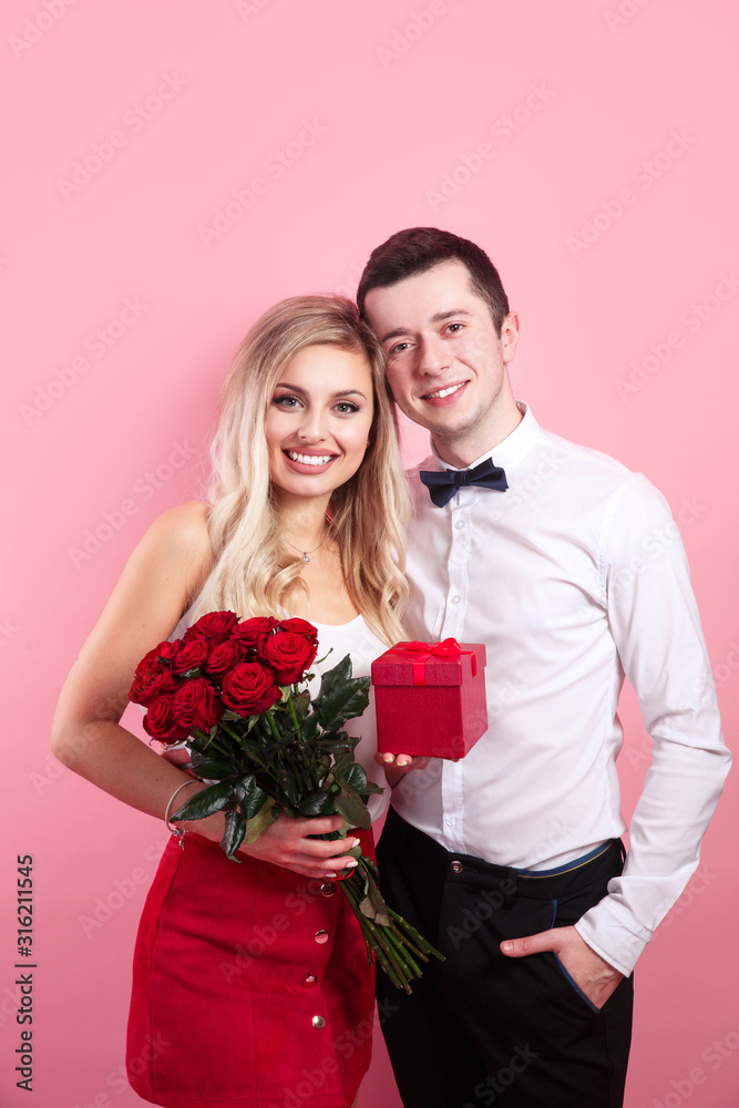 Attractive young woman in dress holding red roses and handsome man in suit are in love Attractive young woman in dress holding red roses and handsome man in suit are in love