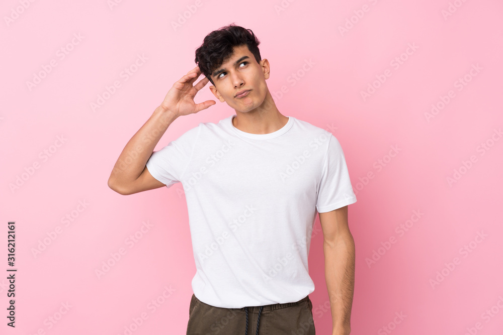 Young Argentinian man over isolated pink background having doubts and with confuse face expression Young Argentinian man over isolated pink background having doubts and with confuse face expression