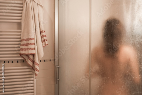 Sexy naked brunette woman take a shower inside the shower cabin seen through foggy glass in her modern design bathroom photo
