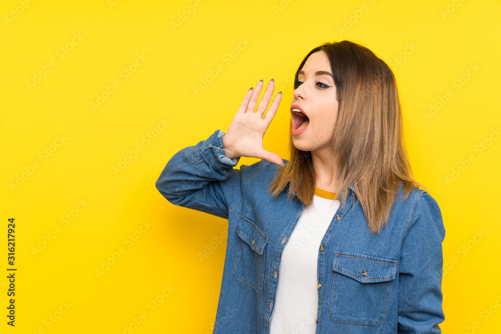 Young woman over yellow background shouting with mouth wide open Young woman over yellow background shouting with mouth wide open
