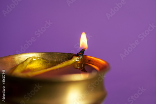 Burning Traditional Brass Diya Or Oil Lamp. Oil lamp burning during Saraswati puja, isolated in violet color background with copy space. Concept for Indian culture, tradition.