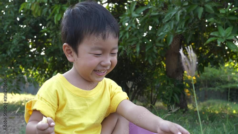 Asian young child boy playing and smiling with happy relaxing face in natural background. Kid in yellow t-shirt laughing. Happy moment. Slow motion close up 4K Asian young child boy playing and smiling with happy relaxing face in natural background. Kid in yellow t-shirt laughing. Happy moment. Slow motion close up 4K