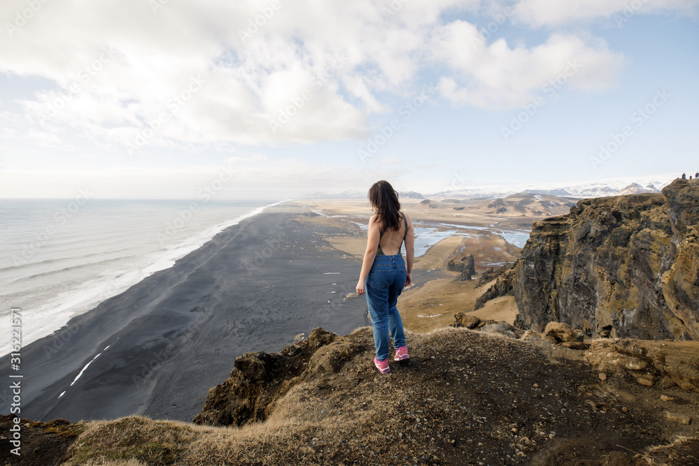 young female traveler near a cliff view of a black beach and the Atlantic Ocean in Iceland