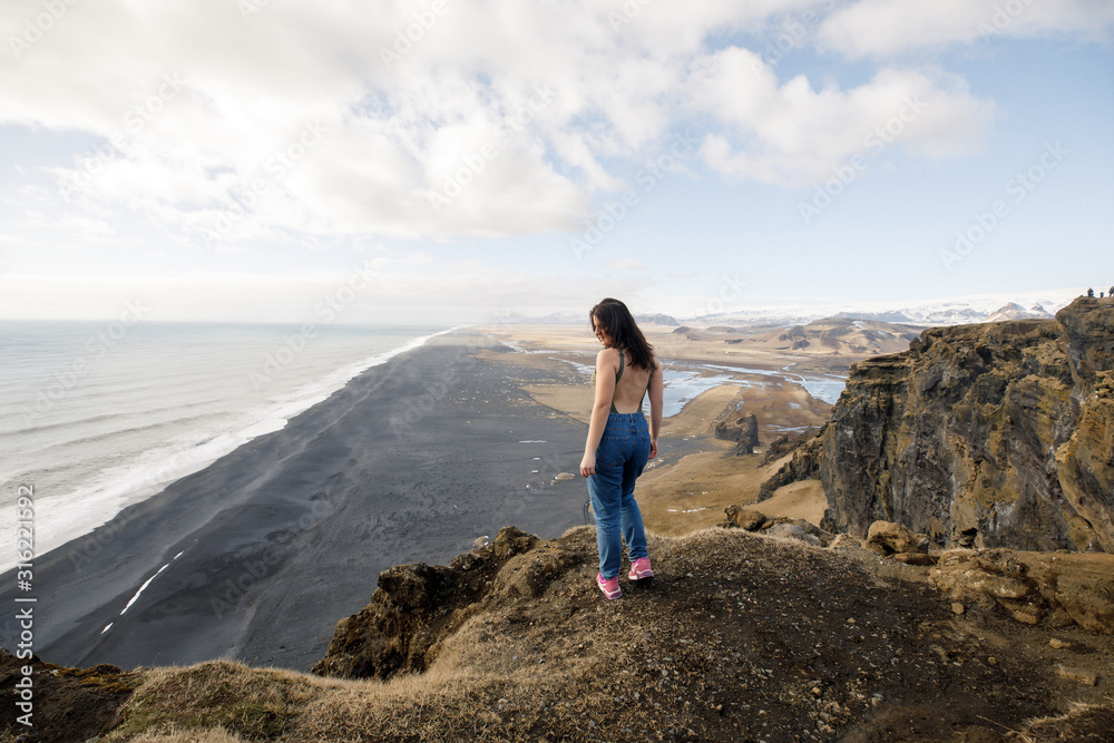 young female traveler near a cliff view of a black beach and the Atlantic Ocean in Iceland