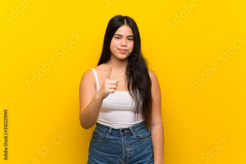 Young teenager Asian girl over isolated yellow background frustrated and pointing to the front