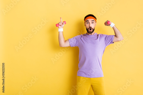 surprised bearded man pointing with finger while holding small dumbbells on yellow © LIGHTFIELD STUDIOS