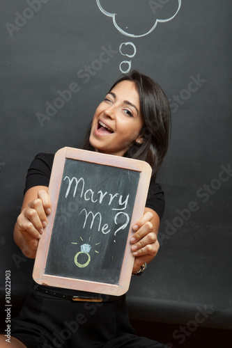 ragazza tiene in mano una tavoletta con su scritto "mi sposi?"