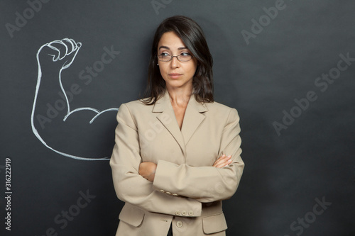 donna con giacca e occhiali ha disegnato dietro di se un braccio muscoloso photo