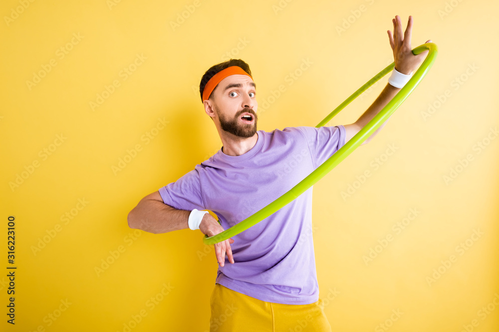confused sportsman exercising with hula hoop on yellow