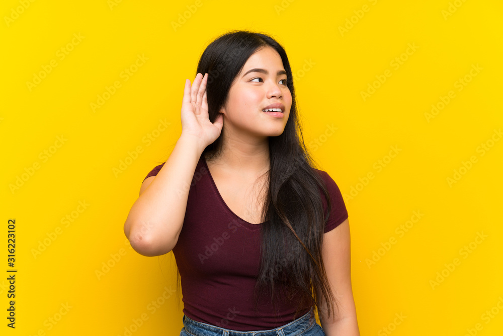 Young teenager Asian girl over isolated yellow background listening something Young teenager Asian girl over isolated yellow background listening something