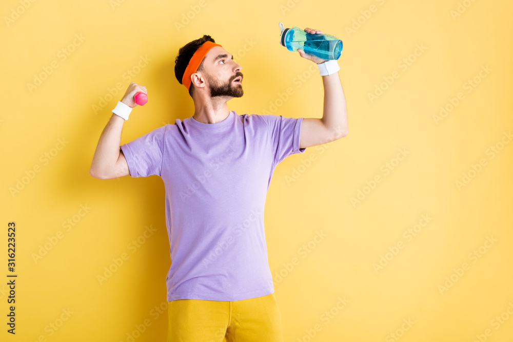 side view of bearded man holding sports bottle while working out with small dumbbell on yellow side view of bearded man holding sports bottle while working out with small dumbbell on yellow