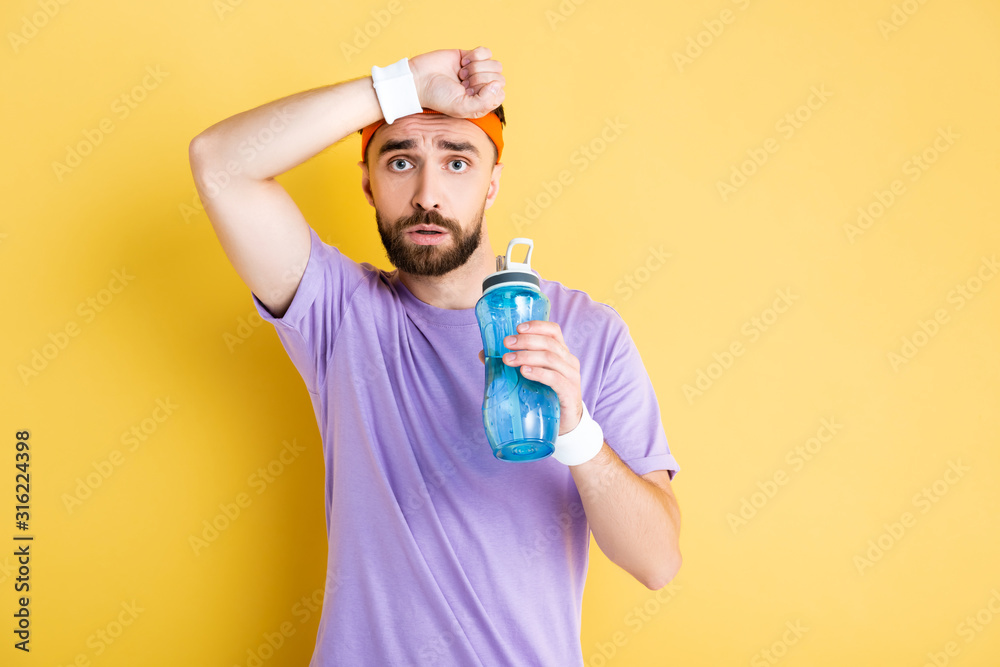 tired sportsman holding sports bottle on yellow