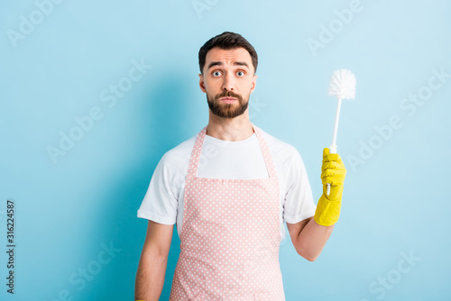 shocked man holding toilet brush and looking at camera on blue photo