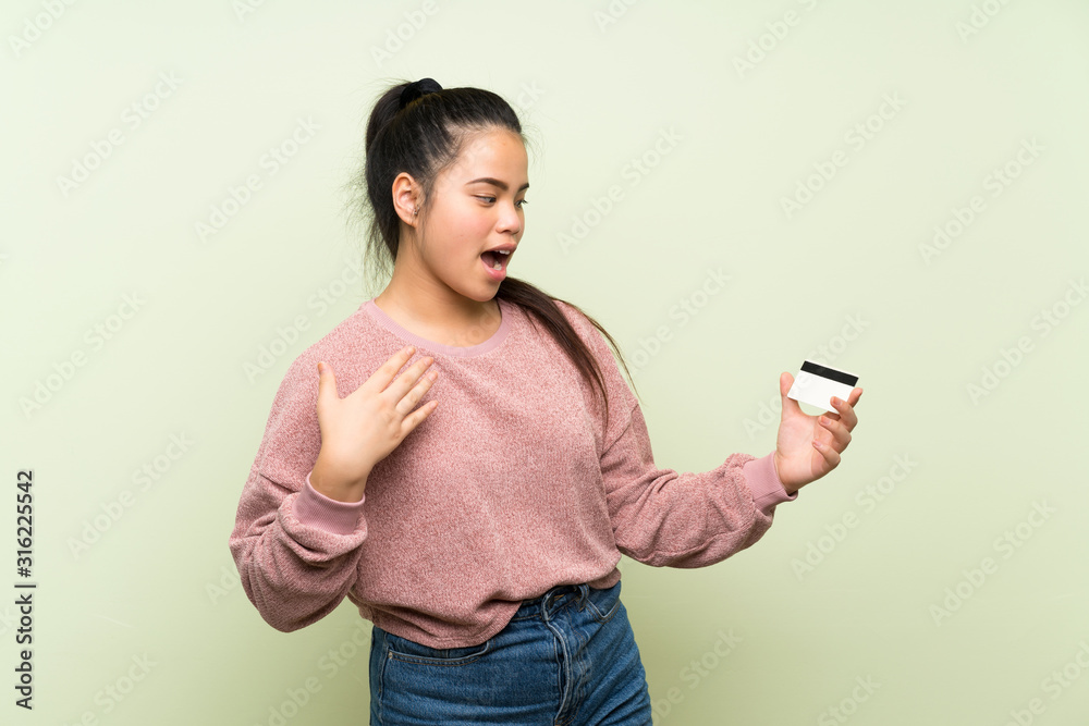 Young teenager Asian girl over isolated green background holding a credit card Young teenager Asian girl over isolated green background holding a credit card