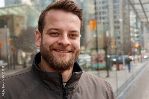 Man with a beard smiling in downtown Toronto with sky rise buildings in the background