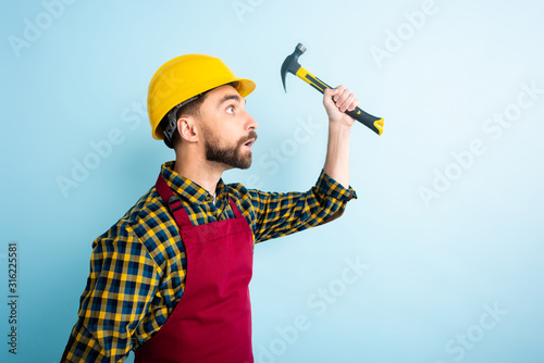 side view of surprised workman holding hummer isolated on blue