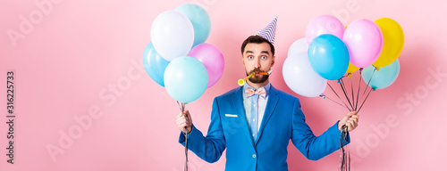 Fotografiet panoramic shot of businessman in party cap holding balloons on pink