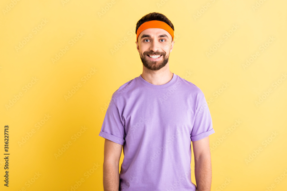 cheerful sportsman in headband smiling isolated on yellow