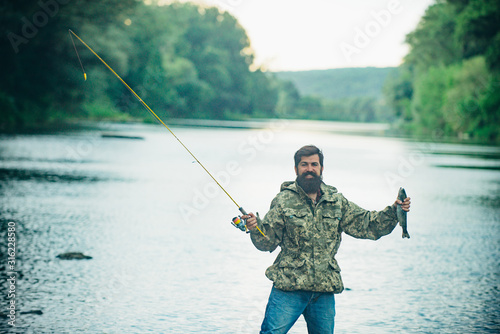 Elegant bearded man fishing. Master baiter. Fishing by the lake. Rest and recreation. Gone fishing. Against the background of the water with a reflection of the forest.