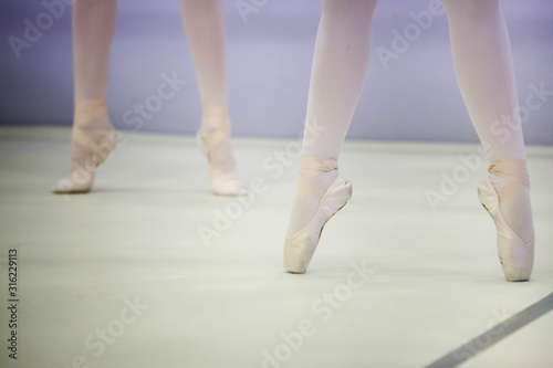  legs of a ballerina in white tights and beige pointes at a training session in the gym © KseniyaK