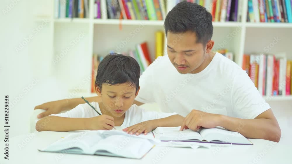 Little boy writing on a book while learning with his father at home. Shot in 4k resolution Little boy writing on a book while learning with his father at home. Shot in 4k resolution