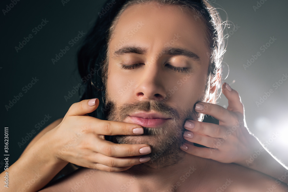 Obraz premium girl touching face of handsome man with closed eyes on grey with back light