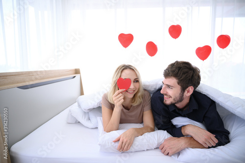 Couple. Love. Valentine's day. Woman is holding red paper hearts and they look at each other with smiling on bed